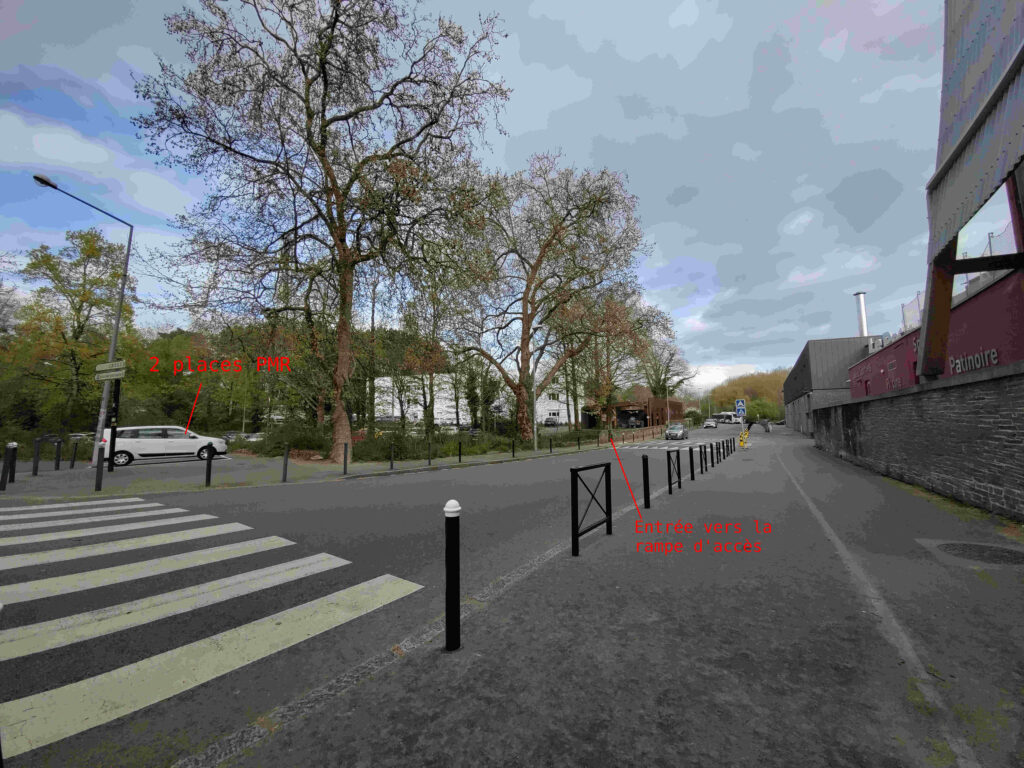 Photo depuis d'extérieur. À gauche il y a les places PMR et sur le même trottoir on appercoit l'entrée pour la rampe d'accès à l'atelier