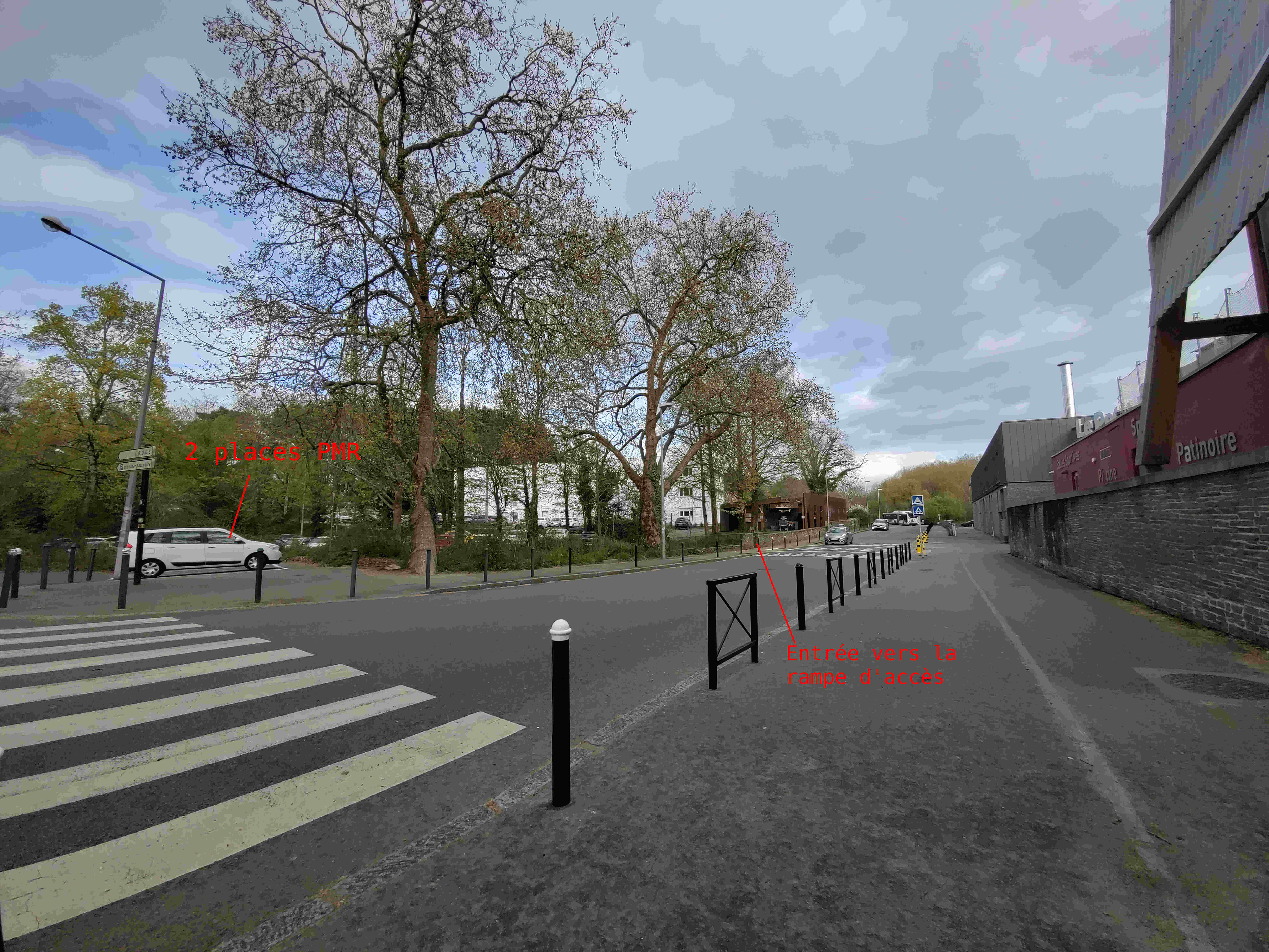 Photo depuis d'extérieur. À gauche il y a les places PMR et sur le même trottoir on appercoit l'entrée pour la rampe d'accès à l'atelier