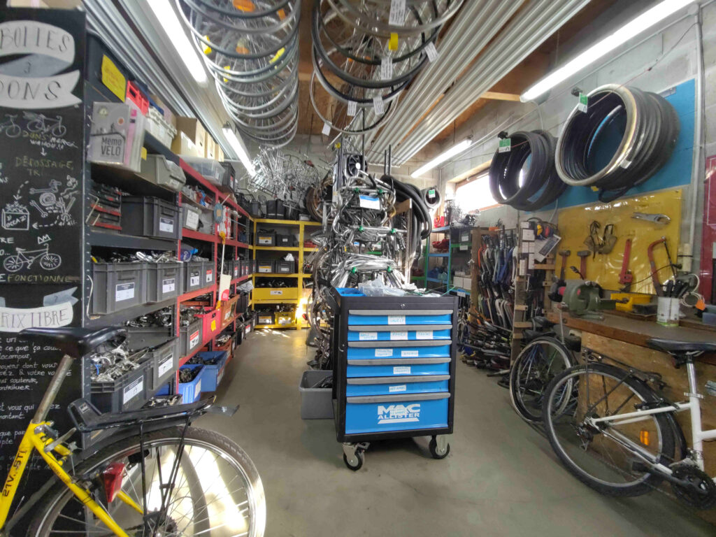 Endroit des pièces d'occasion, entouré d'étagères remplies de bacs de pièces
Au milieu, une desserte à tiroirs et une colonne portant des cintres